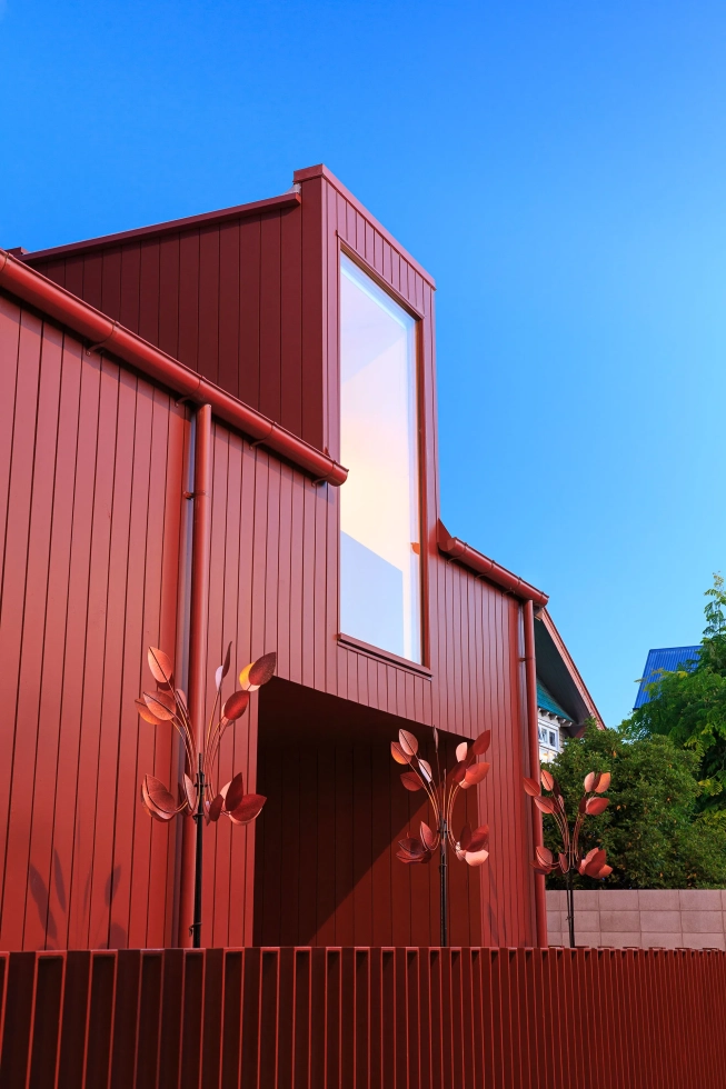 <img title="Architectural facade featuring deep red vertical cladding, a central tall rectangular window, and decorative metal plant sculptures in the foreground." alt="Architectural facade featuring deep red vertical cladding, a central tall rectangular window, and decorative metal plant sculptures in the foreground." src="/images/0/0/5/-/c/005-commercial-photographer-lumo-f51923f7.webp?description" width="960" height="1440" style="--aspect-ratio: 1920/2880;" />